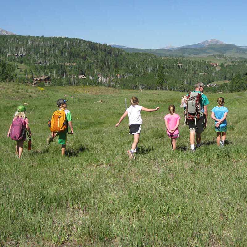 Five kids hiking through grassy field with engaged counselor in Telluride with a view of Lone Cone.